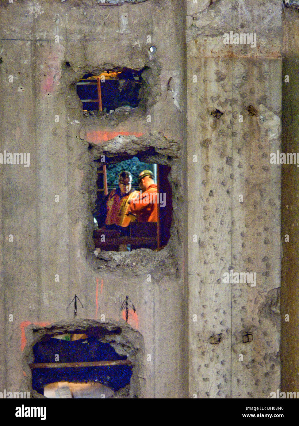 Glimpsed through a hole in a construction wall, two New York City subway workmen confer. Note safety equipment. Stock Photo