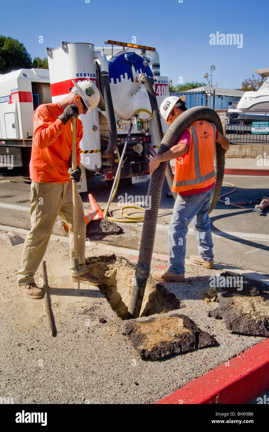 Using a vacuum excavator, two workmen uncover an underground utility