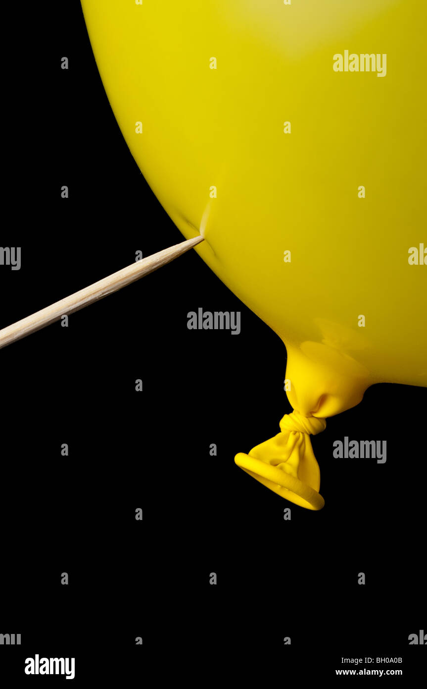 a pointed stick ready to pop a yellow balloon on black Stock Photo