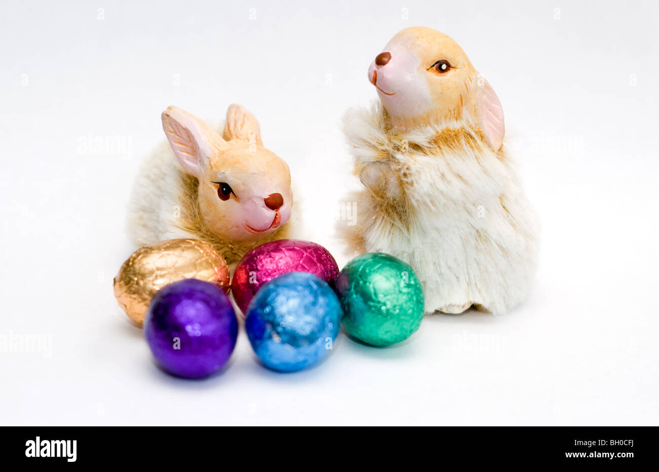 Two rabbit ornaments with a small selection of colorful mini chocolate Easter eggs on a white background Stock Photo