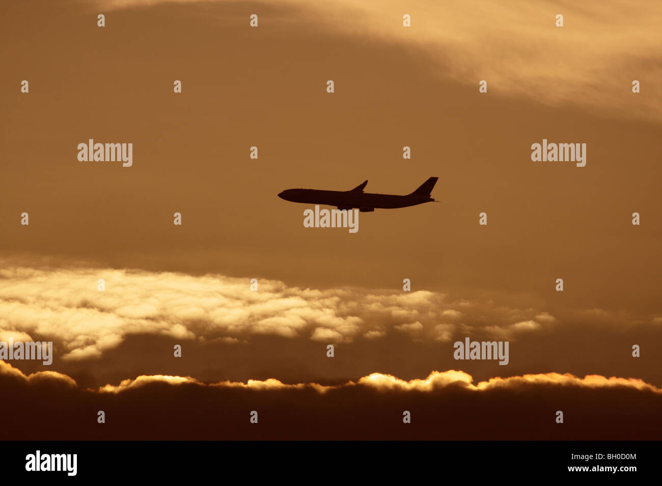 Air travel. Commercial passenger jet plane flying in the air against a cloudy sky at sunset. Silhouette of airplane in flight path. Civil aviation. Stock Photo