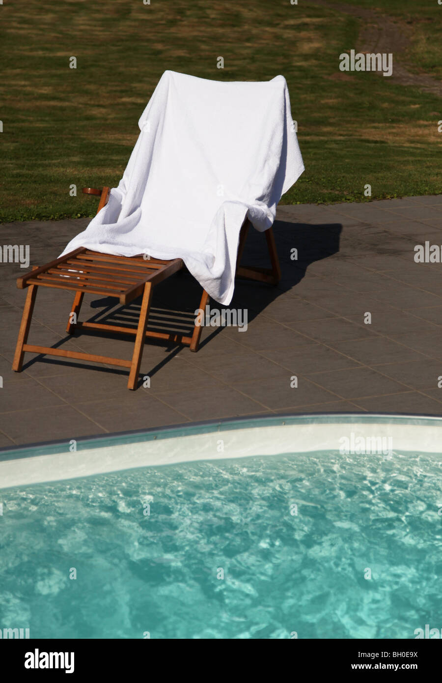 A standard deck chair standing next to a swimming pool. Stock Photo