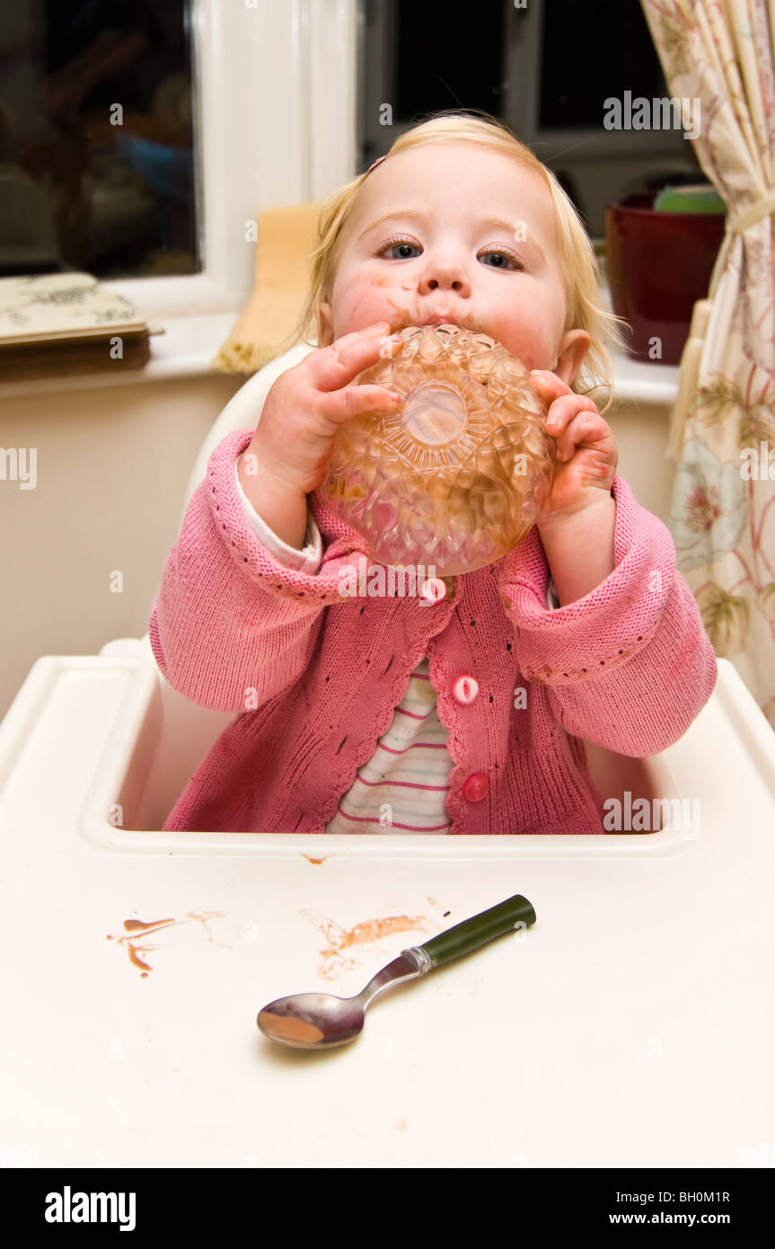 Vertical close up portrait of a baby girl getting in a mess putting her bowl of chocolate ice cream on her head Stock Photo