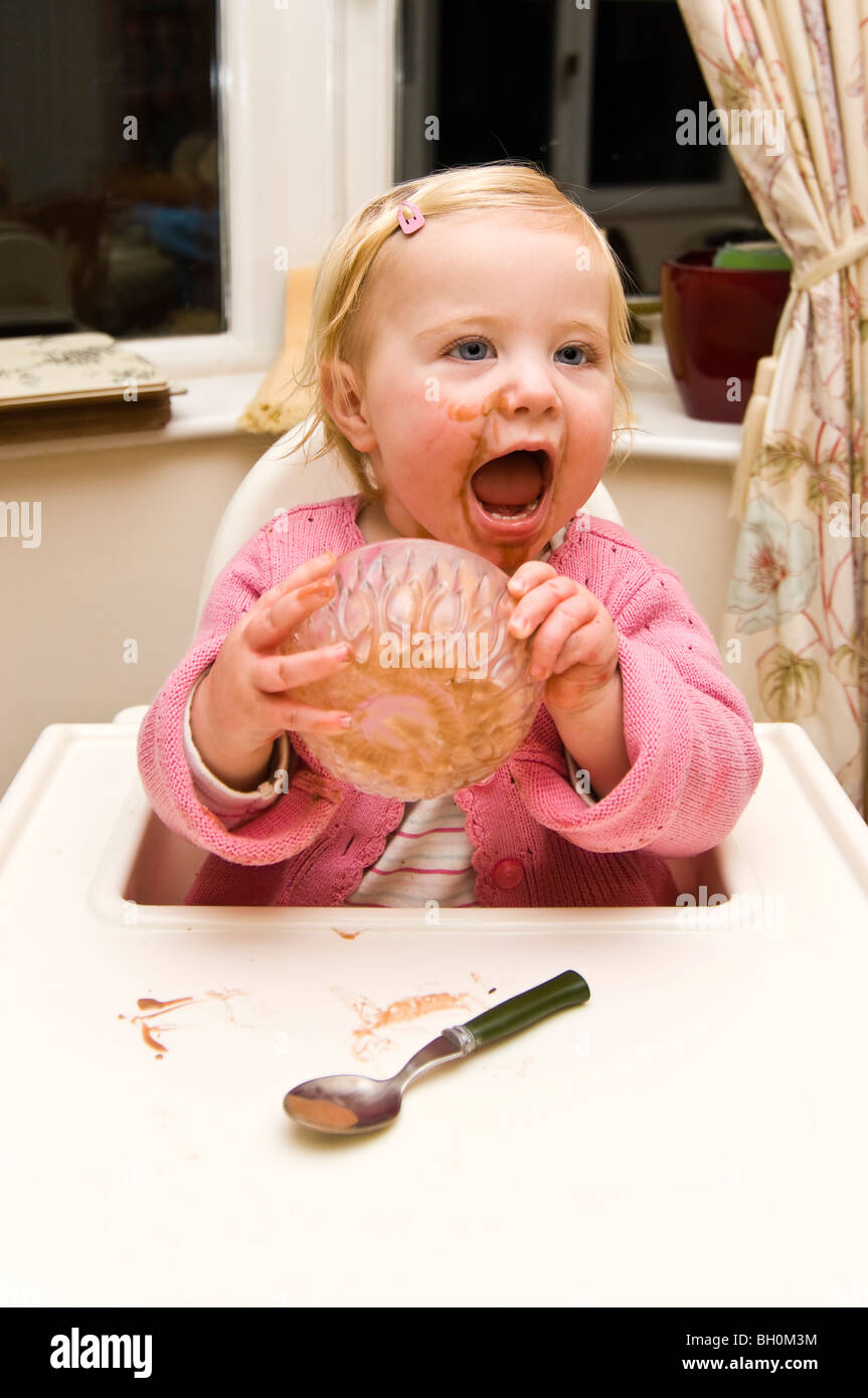 Vertical close up portrait of a baby girl getting in a mess putting her bowl of chocolate ice cream on her head Stock Photo