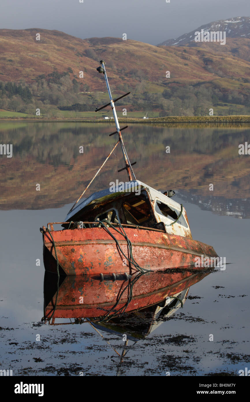 Half sunken fishing boat in a Scottish Loch reflected in its mirror-like water with the  hills of the Highlands in background Stock Photo
