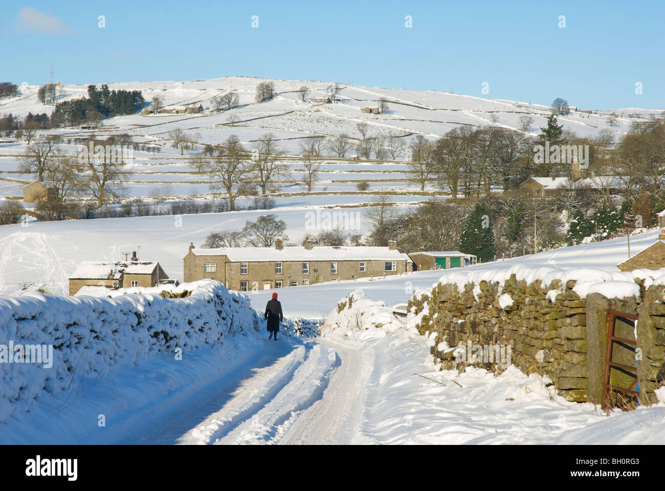 Woman walking along snowy road in Wharfedale, Yorkshire Dales National Park, England UK Stock Photo