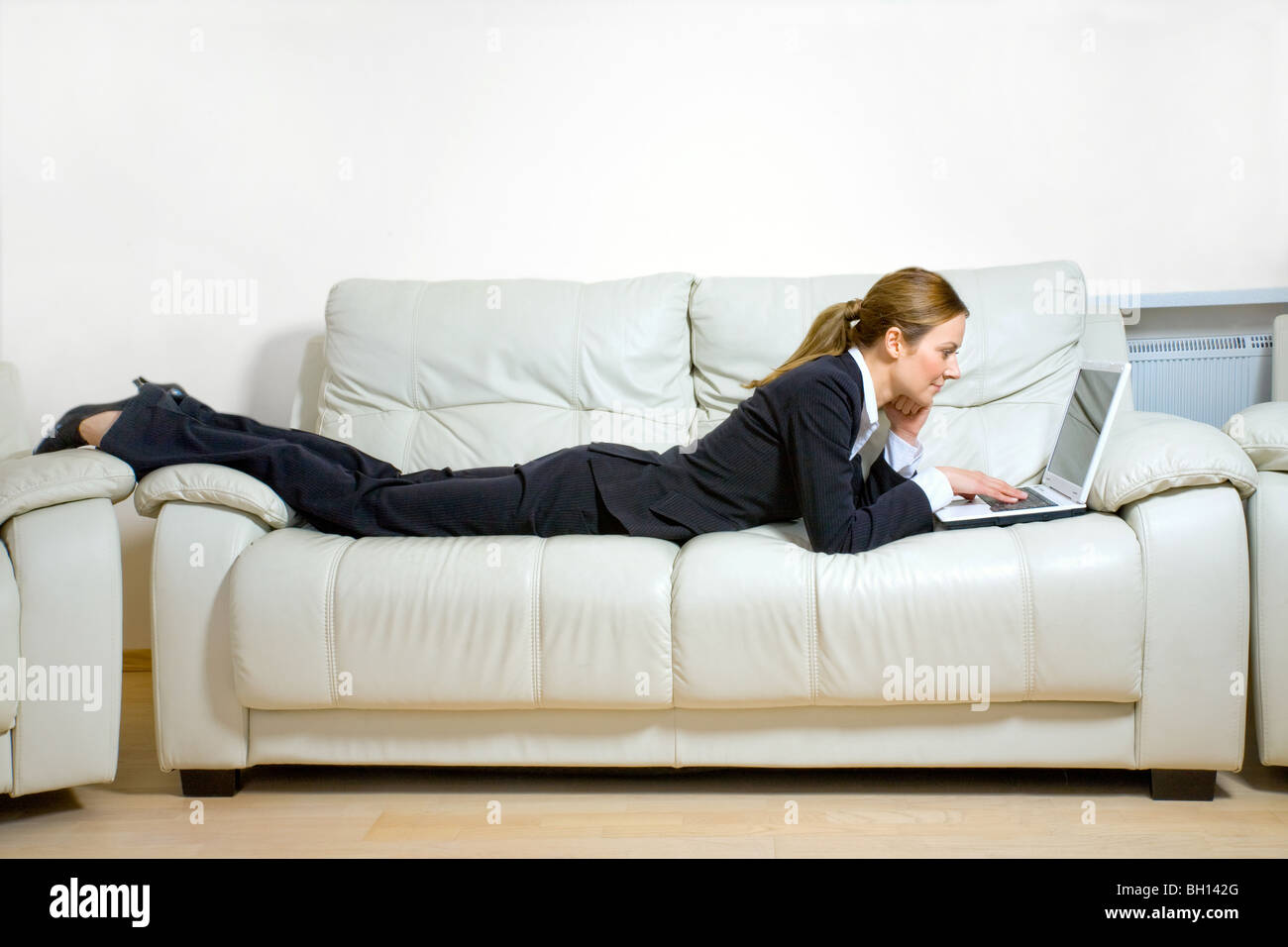 Business woman with laptop lying on a couch Stock Photo - Alamy