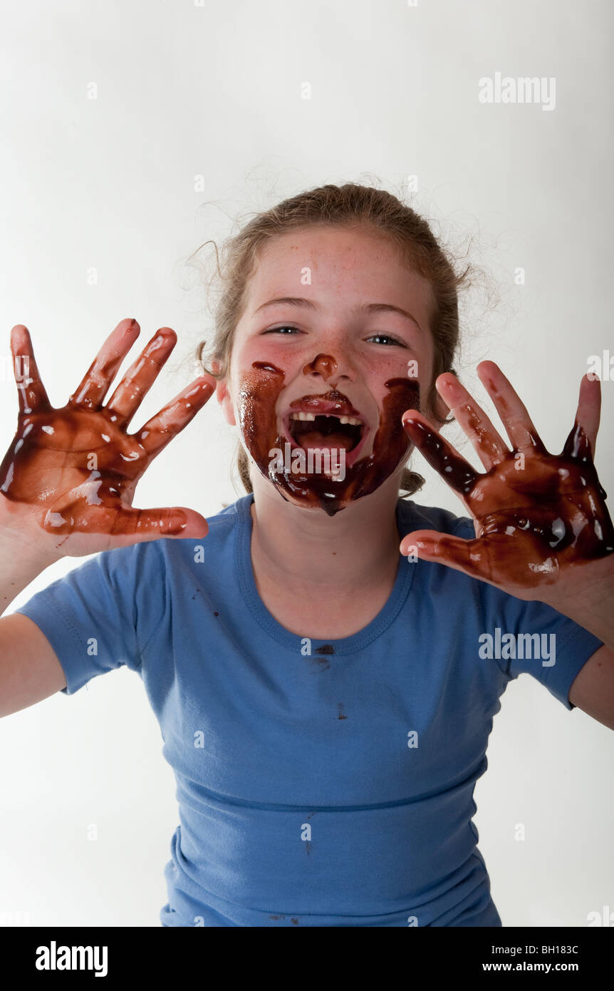 little girl (7 years old) laughing with face and hands covered in chocolate white background Stock Photo