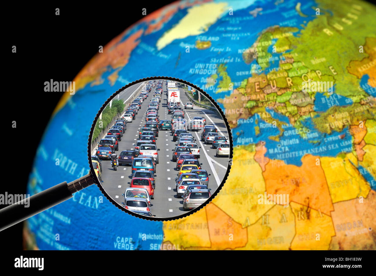 Cars in traffic jam on motorway during summer holidays seen through magnifying glass held against illuminated terrestrial globe Stock Photo