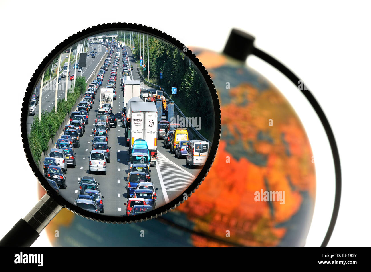 Cars in traffic jam on motorway during the summer holidays seen through magnifying glass held against illuminated globe Stock Photo