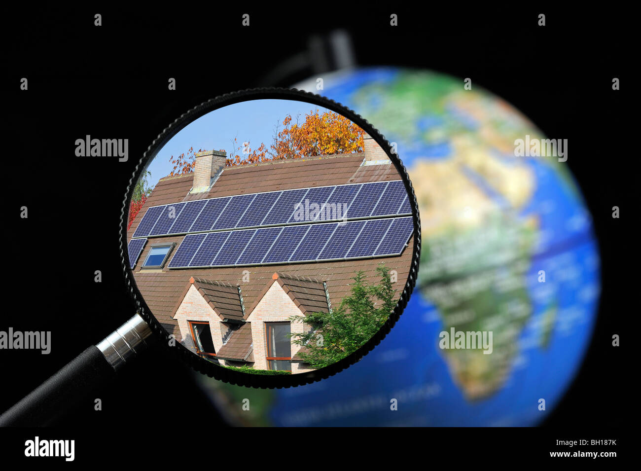 Photovoltaic solar panels / cells on roof of house seen through magnifying glass held against illuminated terrestrial globe Stock Photo