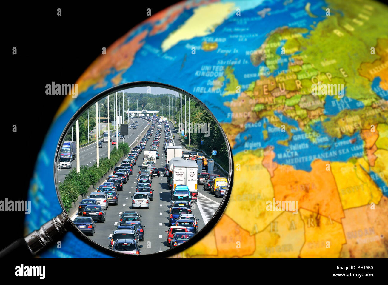 Cars in traffic jam on motorway during summer holidays seen through magnifying glass held against illuminated terrestrial globe Stock Photo