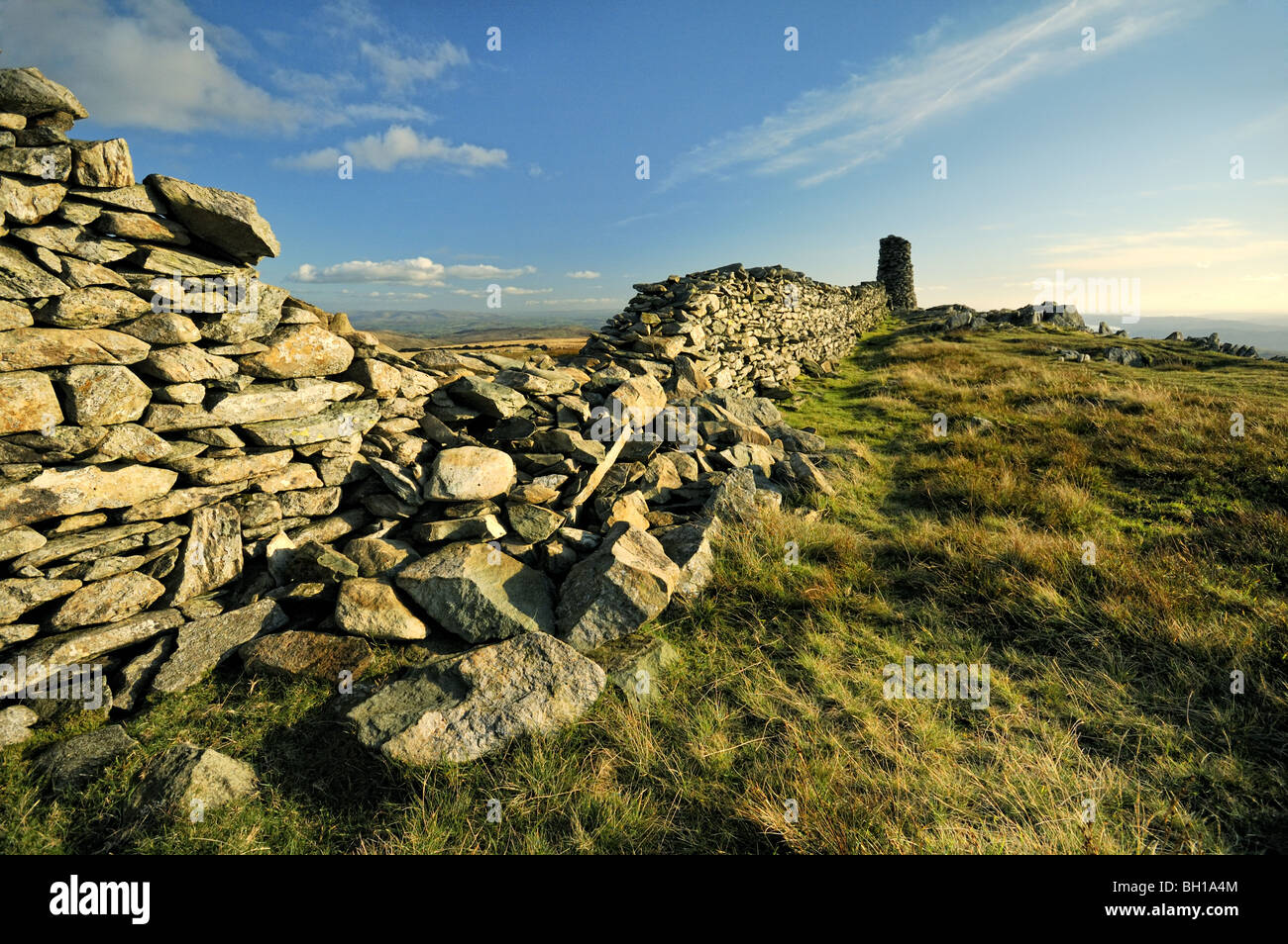 Summit of  'High Street' in the Cumbrian hills with view of a very large cairn at the end of a damaged drystone wall. Stock Photo