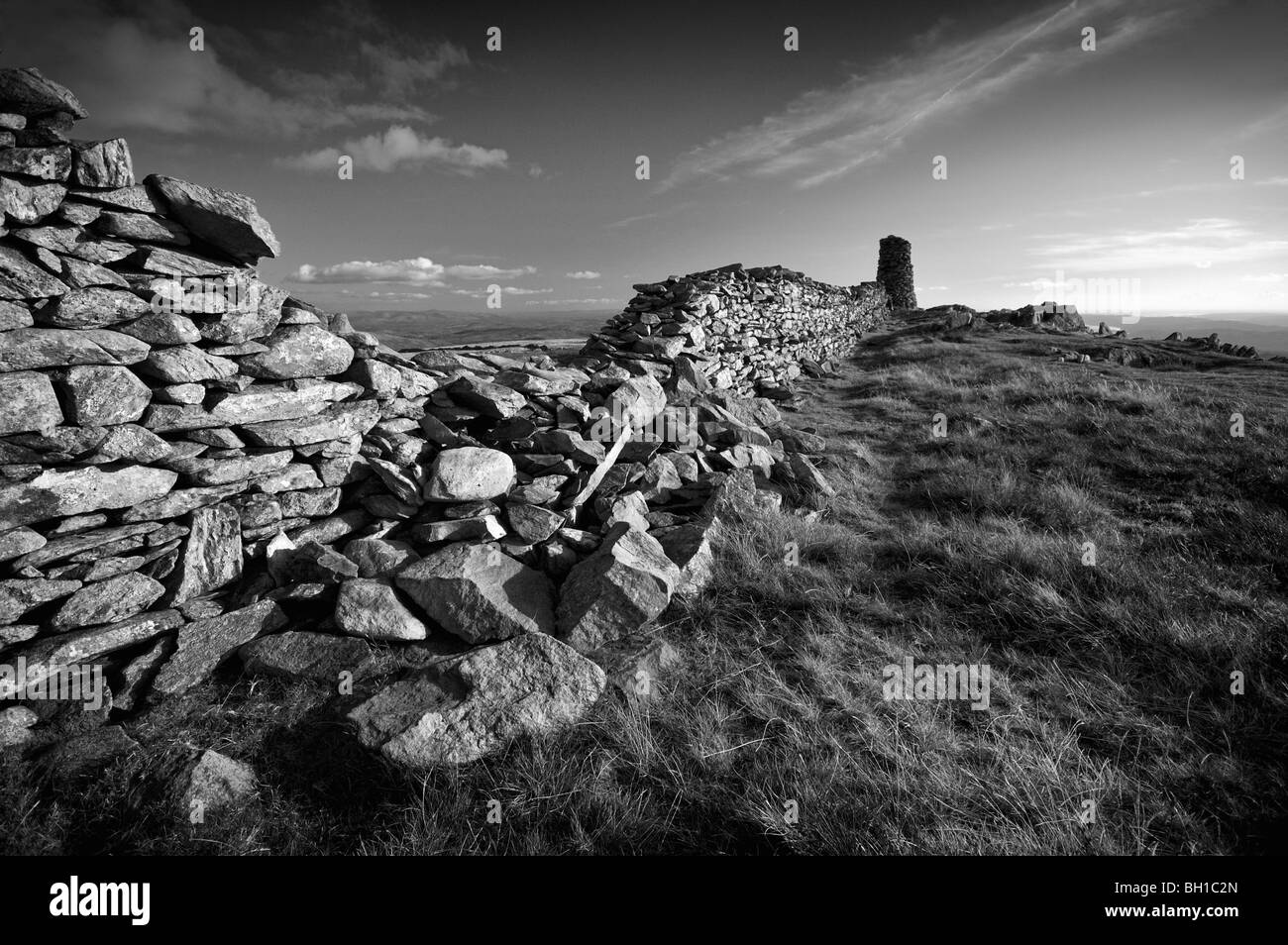 Summit of  'High Street' in the Cumbrian hills with view of a very large cairn at the end of a damaged drystone wall. Stock Photo