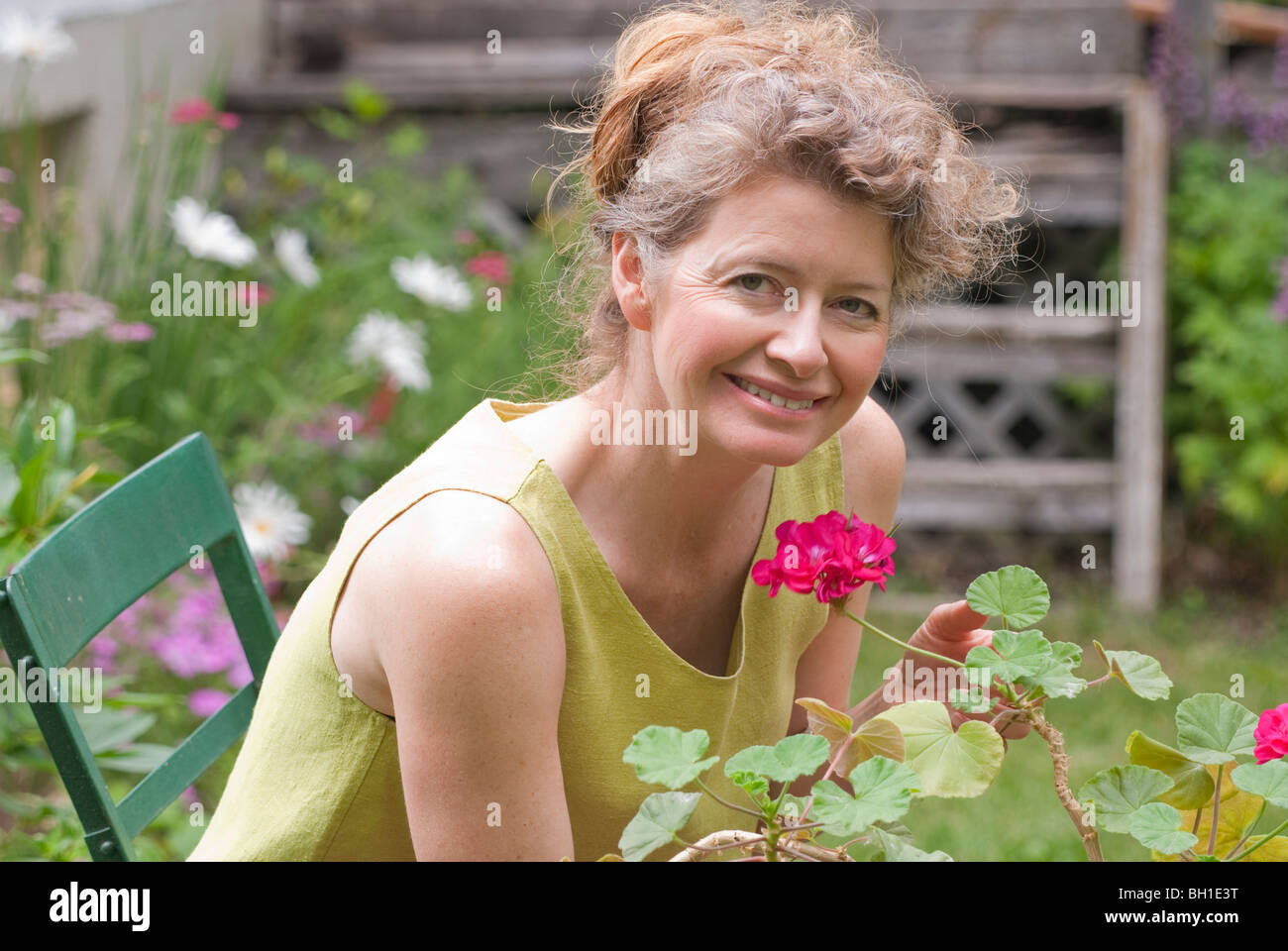 Woman in mid 50s seated in garden holding geranium, Manitoba, Canada Stock Photo