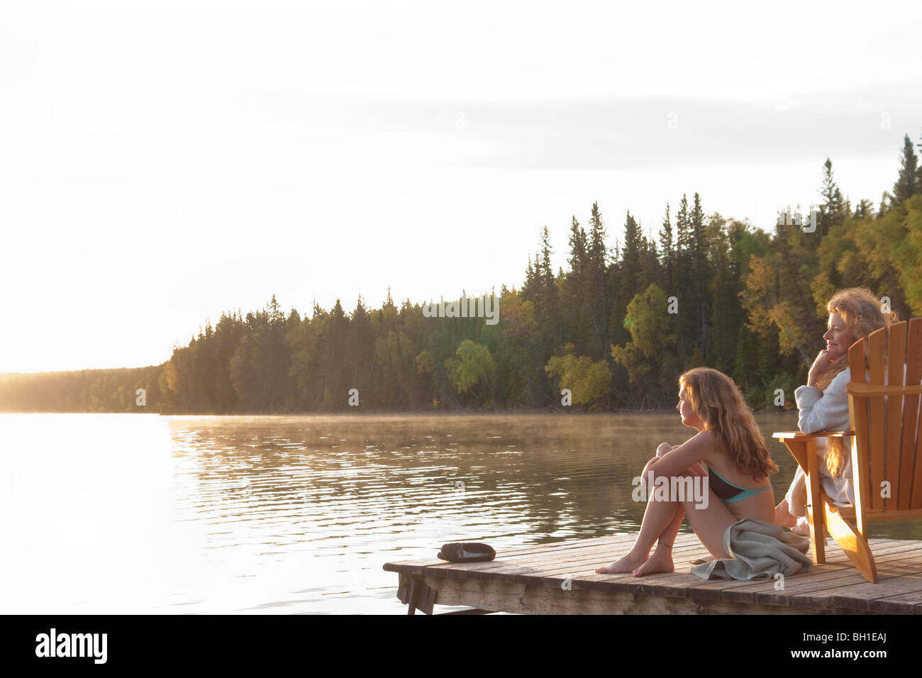 Two women seated on dock at sunset, Clear Lake, Manitoba, Canada Stock Photo