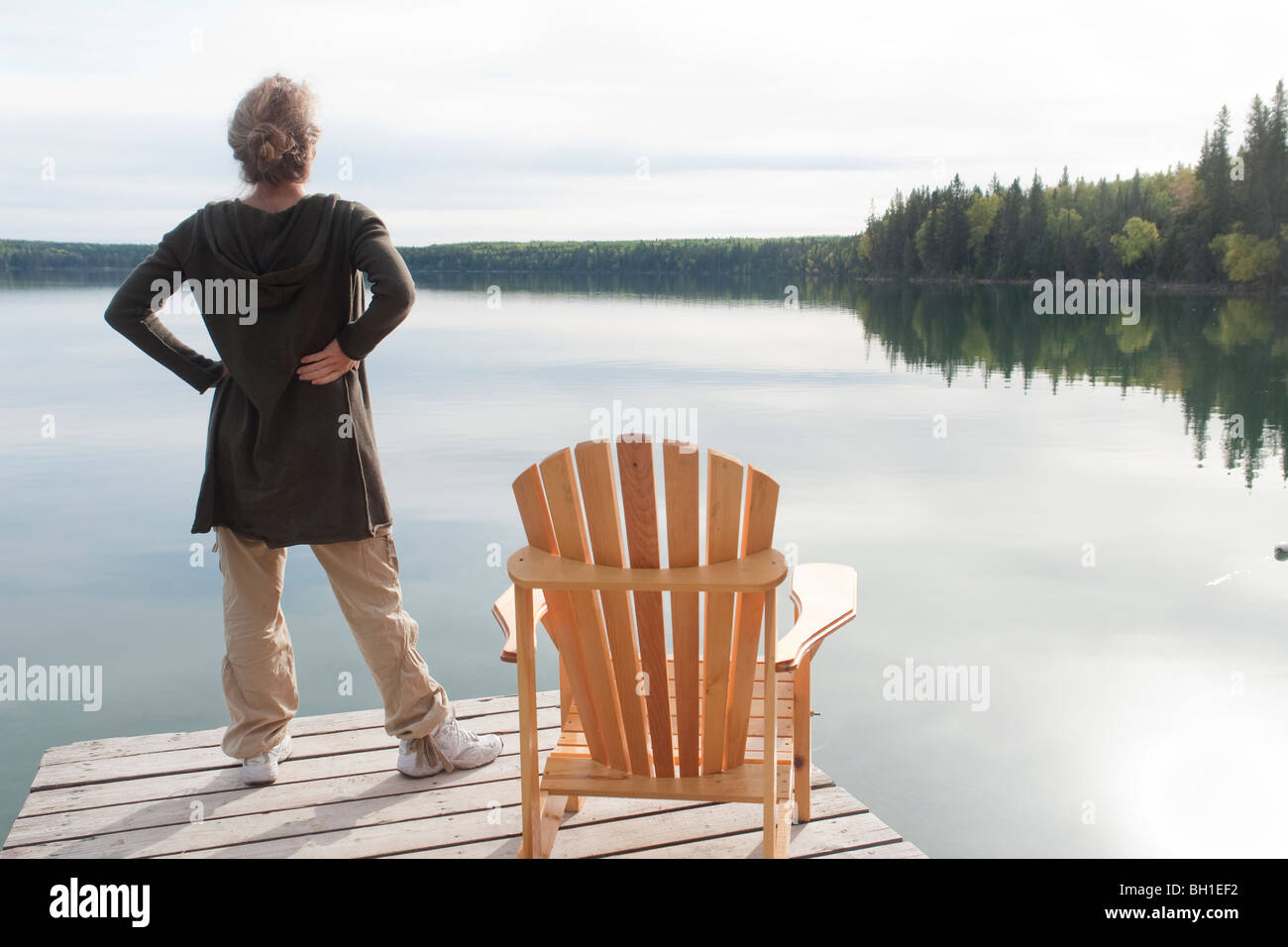 Woman standing on dock beside deck chair, Clear Lake, Manitoba, Canada Stock Photo