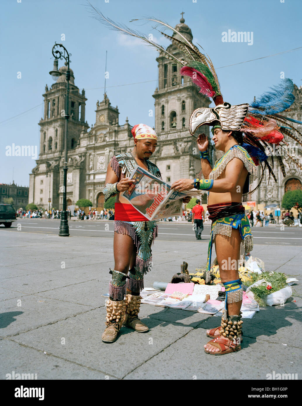 Men wearing aztec costumes reading a newspaper at the Zocalo in front