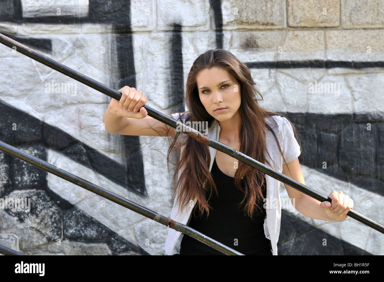 Young cool woman (teenage girl) portrait holding rail in front of black and white graffity wall Stock Photo