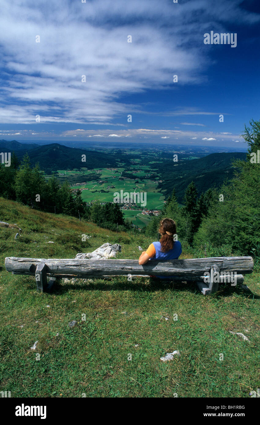 Young woman sitting on bench near alpine hut Kohleralm, view to Inzell, Kohler-Alm, Chiemgau range, Chiemgau, Bavarian foothills Stock Photo