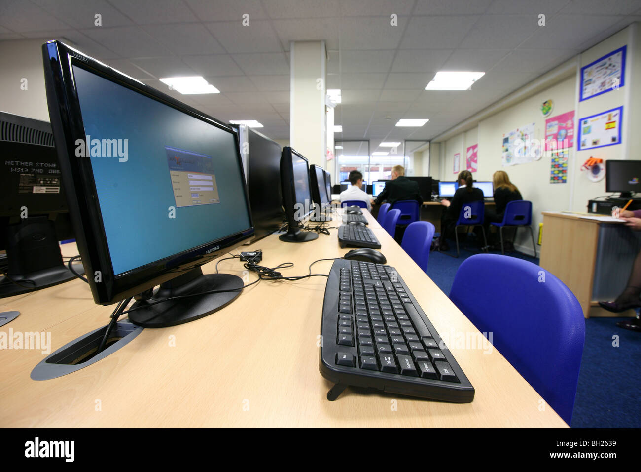 Row of computer monitors and keyboards with children in the background Stock Photo