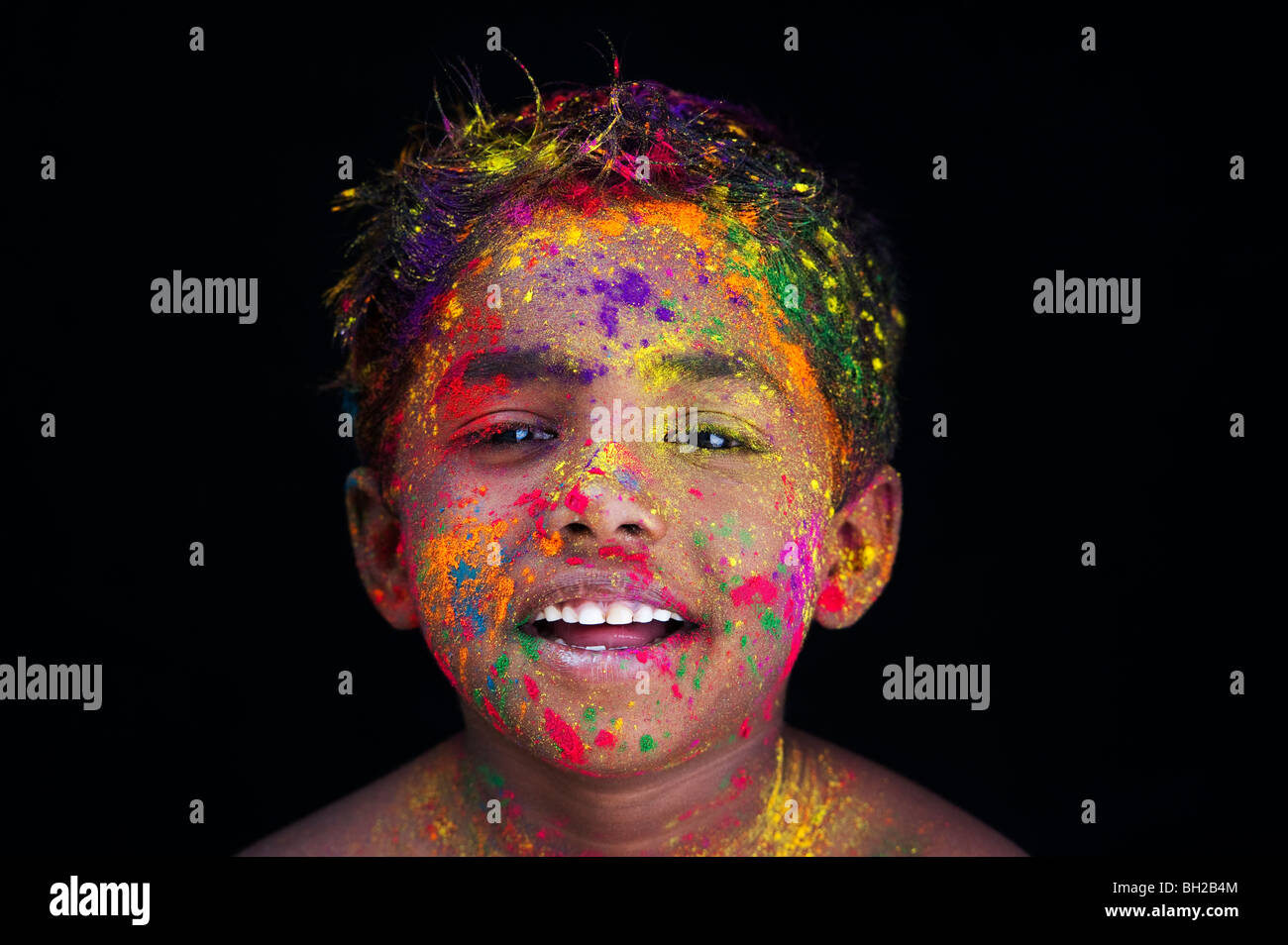Happy young Indian boy covered in coloured powder pigment against a black background. India Stock Photo