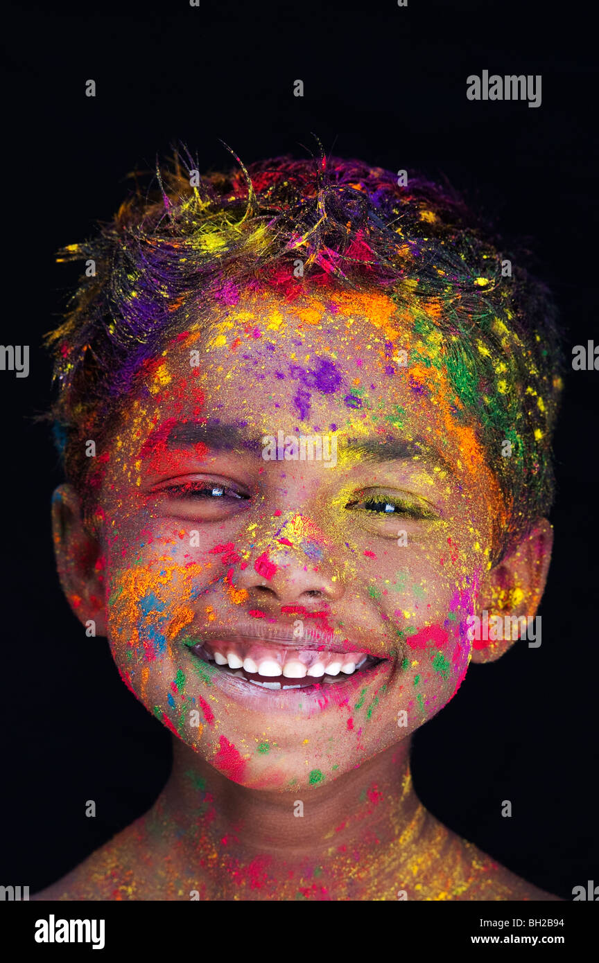 Happy young Indian boy covered in coloured powder pigment against a black background. India Stock Photo