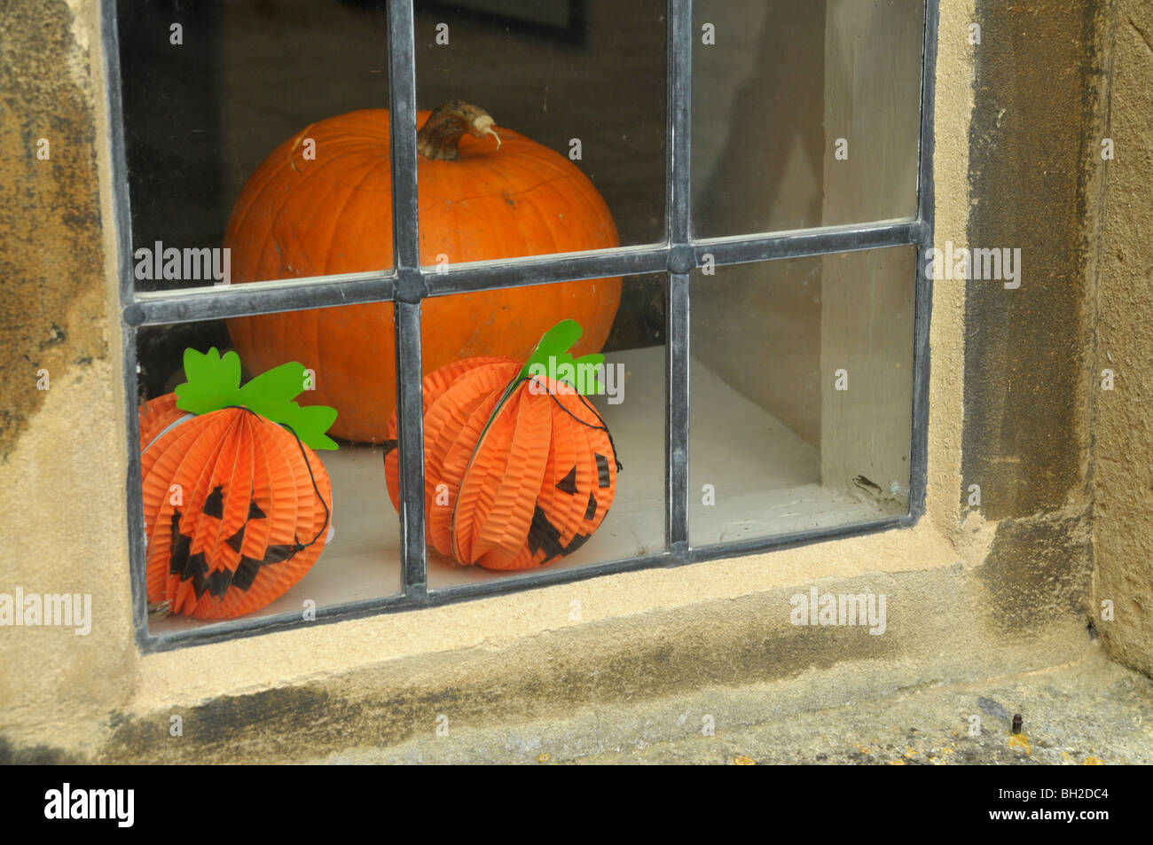 Halloween paper pumpkins with smiley faces  sit on a shop window ledge beside a real one. Stock Photo