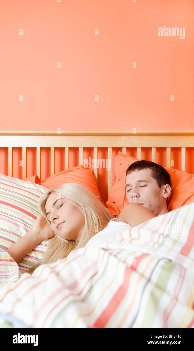 Young couple sleep closely together under a striped bedspread. Vertical
