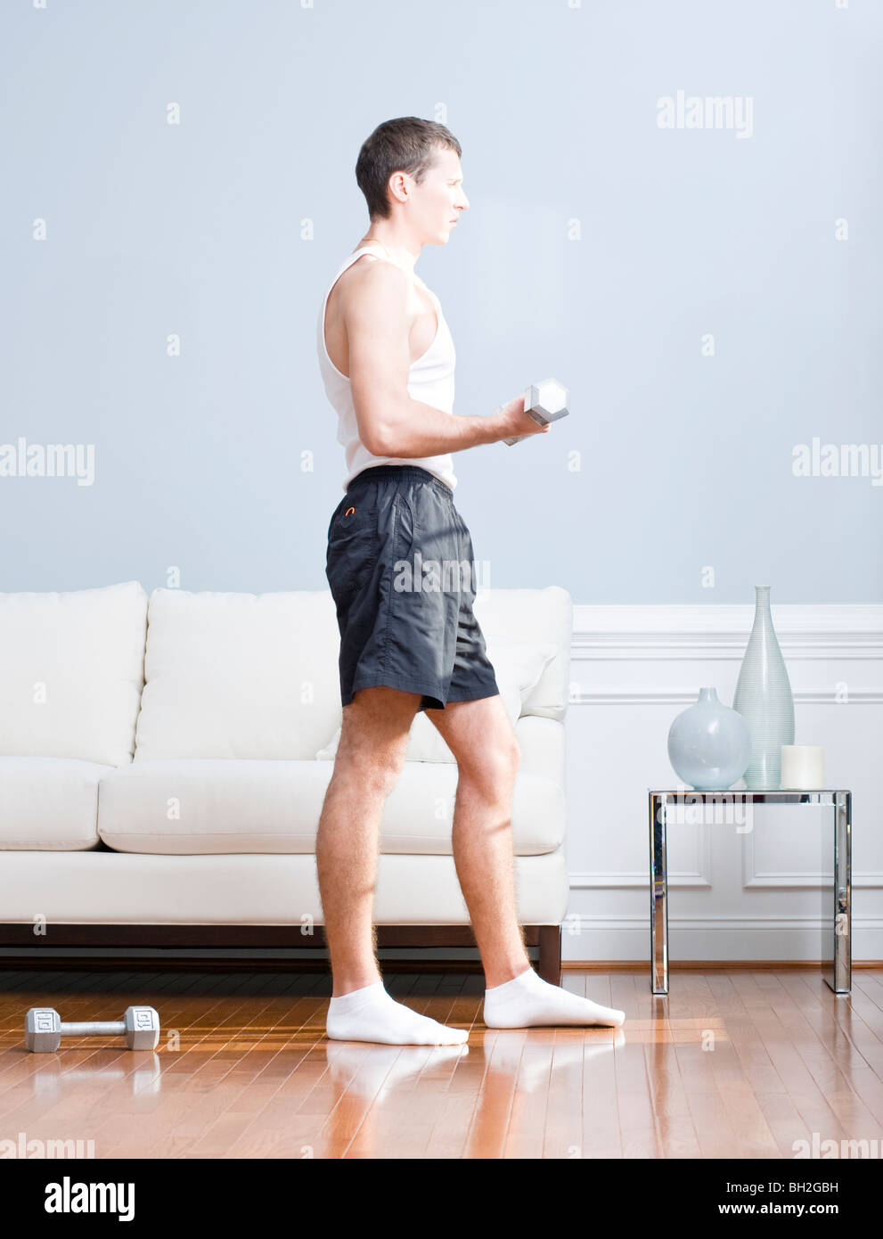 Man using arm weight in his living room as another lies on the floor next to him. Vertical format. Stock Photo