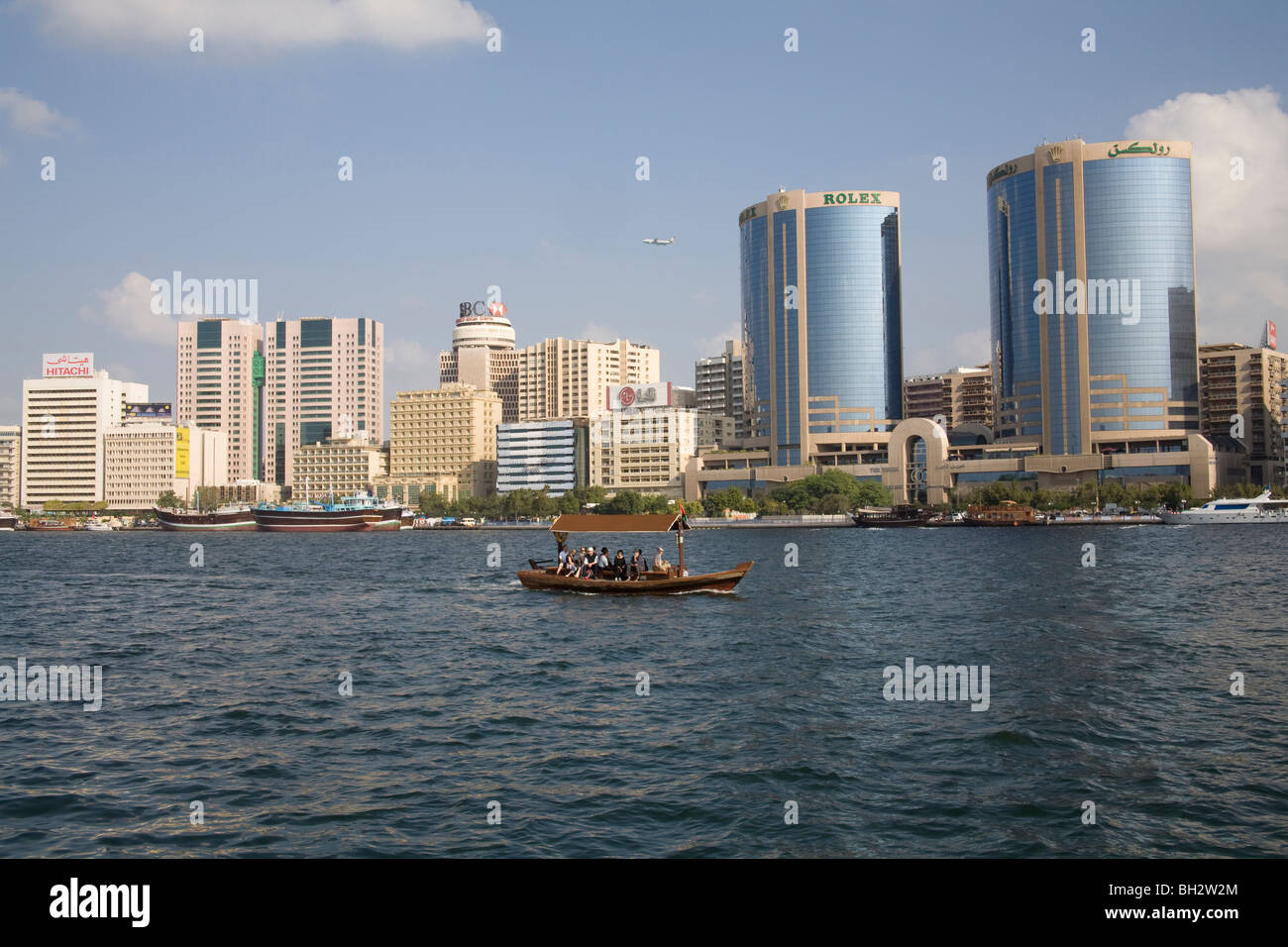 Dubai United Arab Emirates View across Dubai Creek to iconic buildings of Deira City with an abra taking tourists along waterway Stock Photo