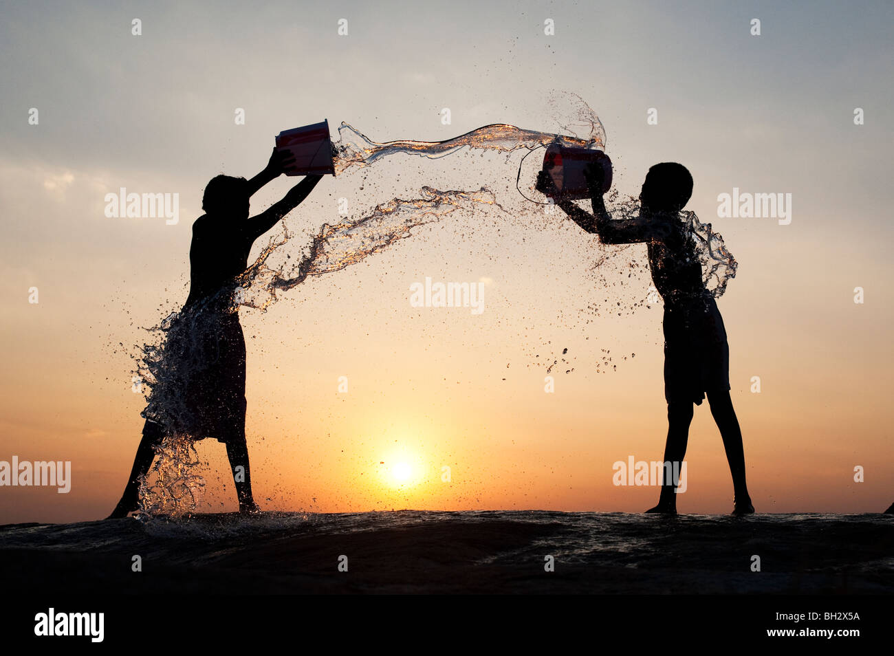 Indian boys throwing water at each other from buckets at sunset. Andhra