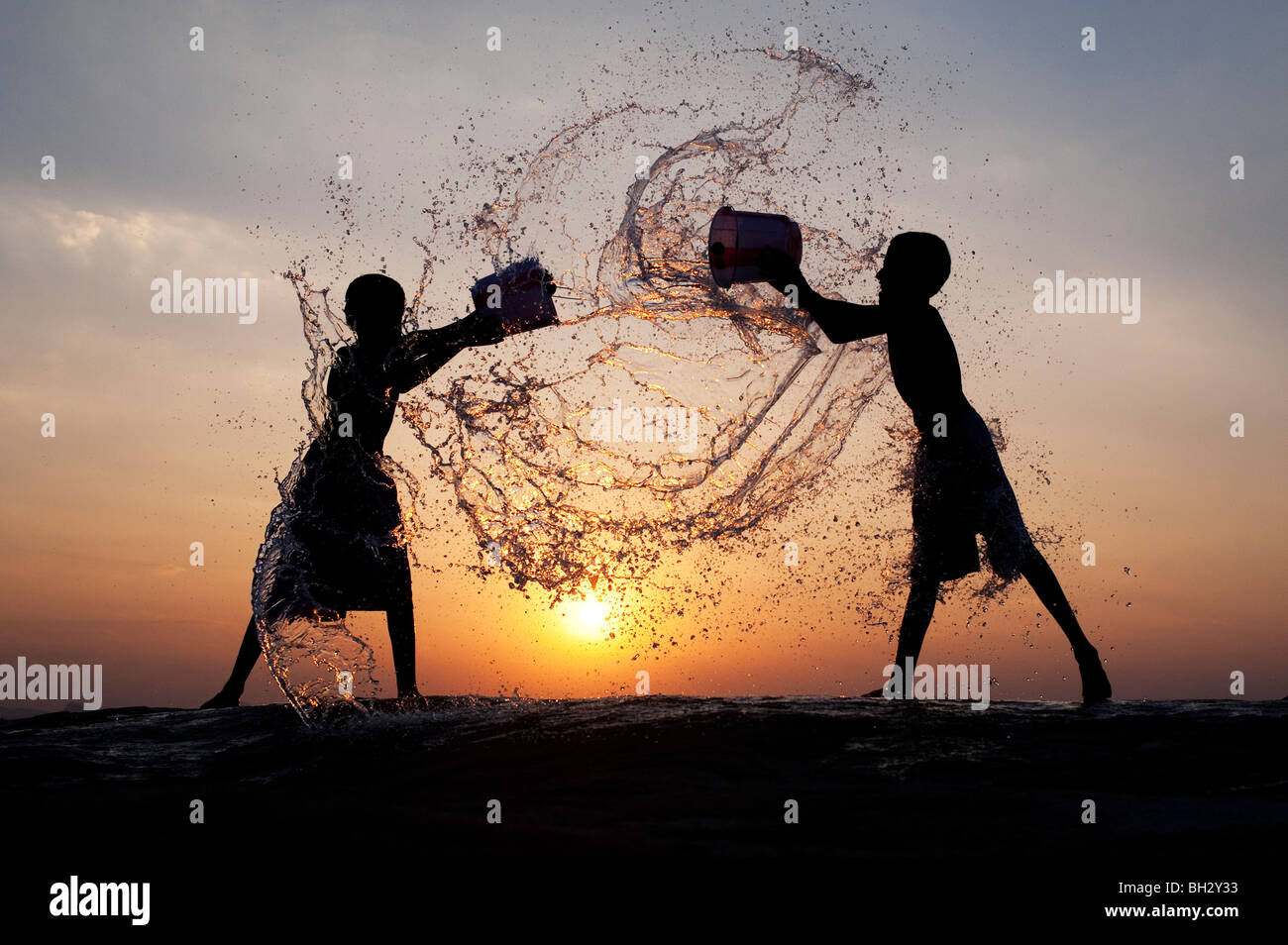 Indian boys throwing water at each other from buckets at sunset. Andhra