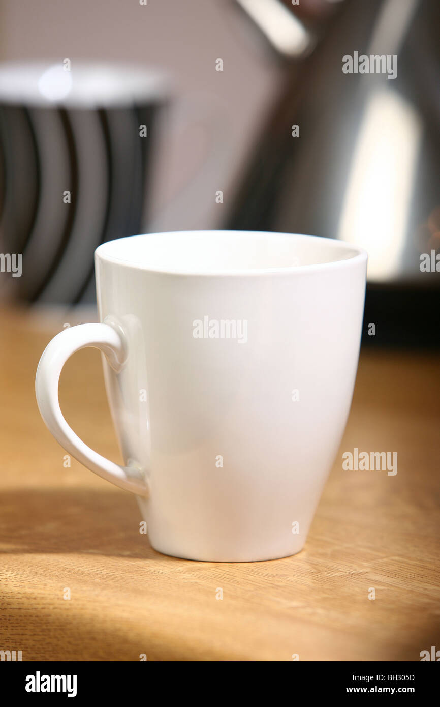 White mug on a kitchen surface (kettle and black mug in the background out of focus) Stock Photo