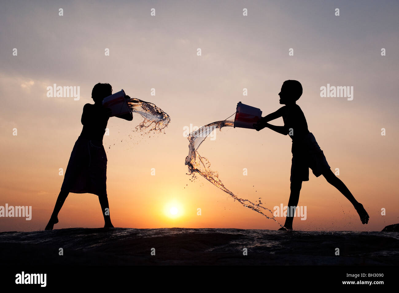 Indian boys throwing water at each other from buckets at sunset. Andhra