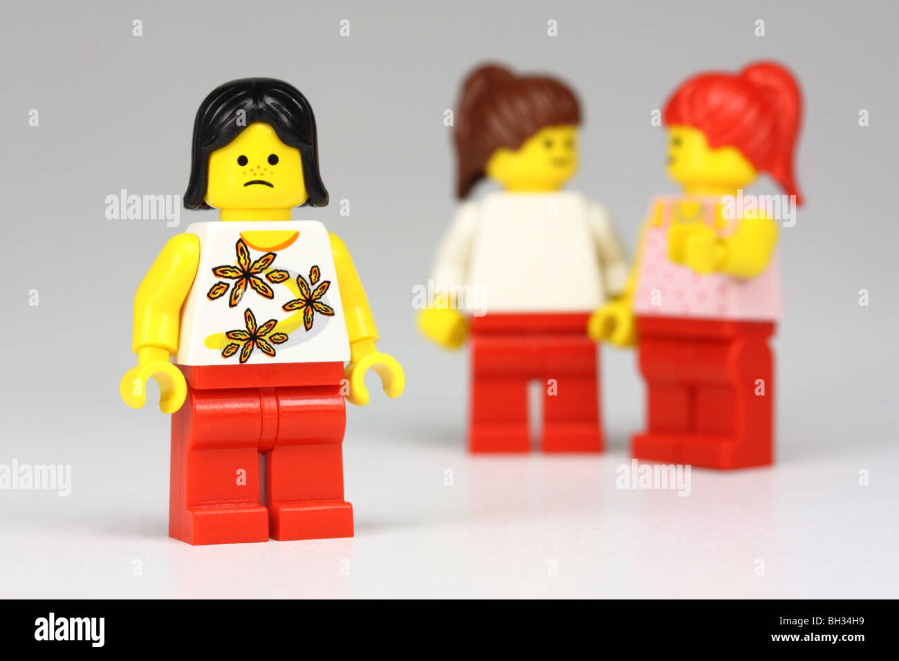 Unhappy lego girl, with 2 other lego girls talking about her behind her back :  isolation/bullying concept Stock Photo
