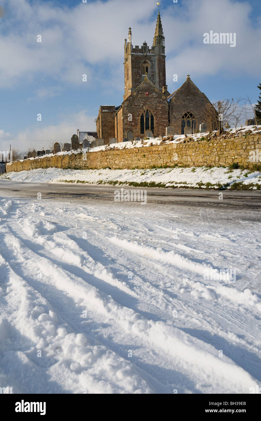 View of country parish church above a road and snow on the ground with tracks in it Stock Photo