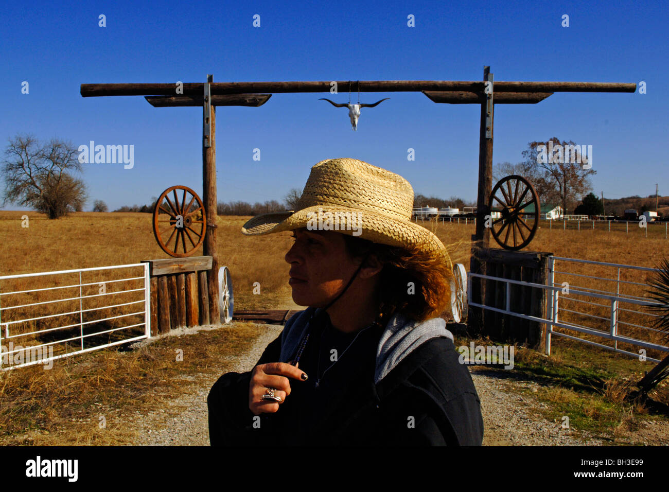 A minority woman surveys the country side while standing in front of a rustic wooden gateway as she works as a cattle rancher Stock Photo