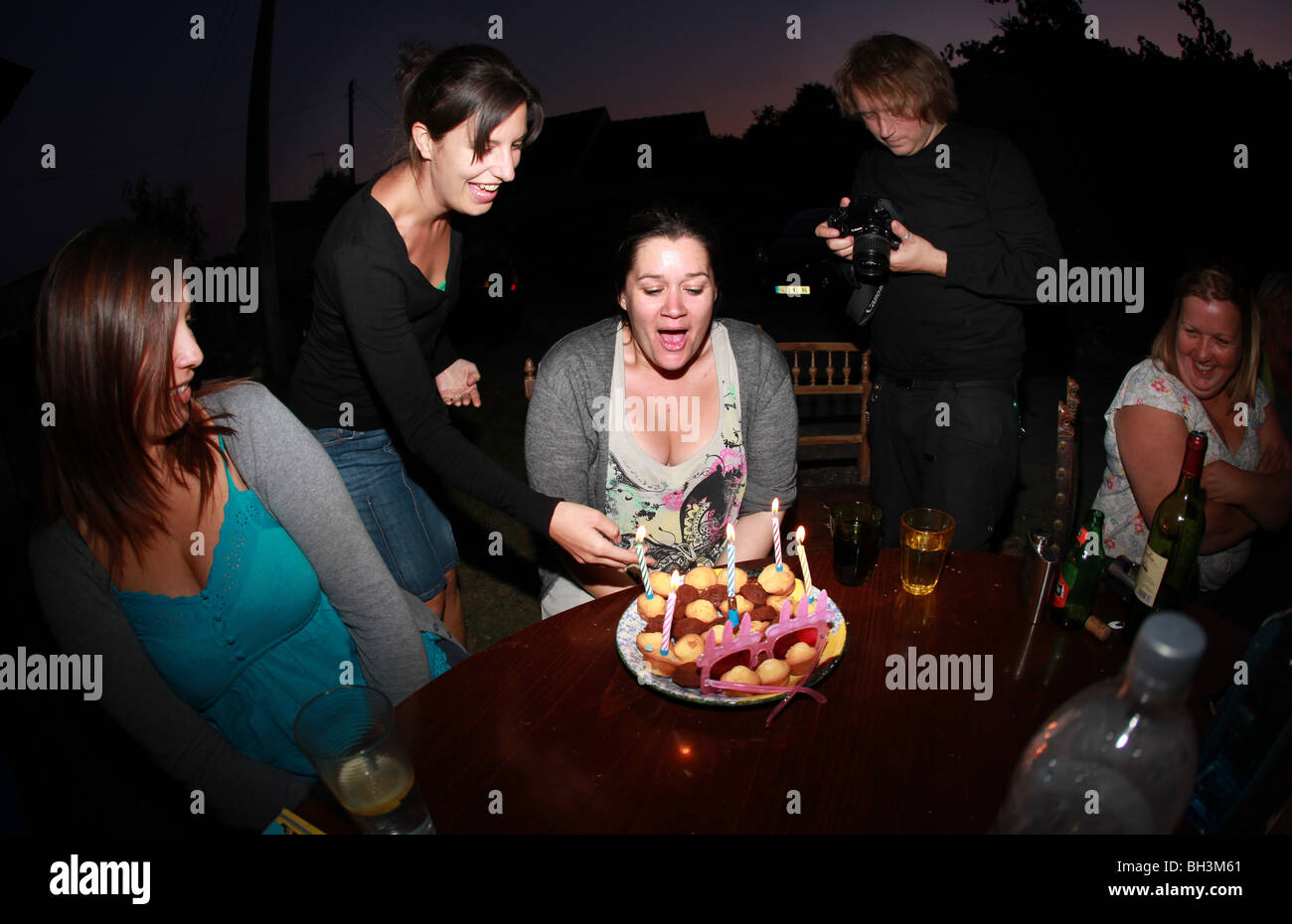 Group of young adults celebrating with a birthday cake outdoors at night. Stock Photo