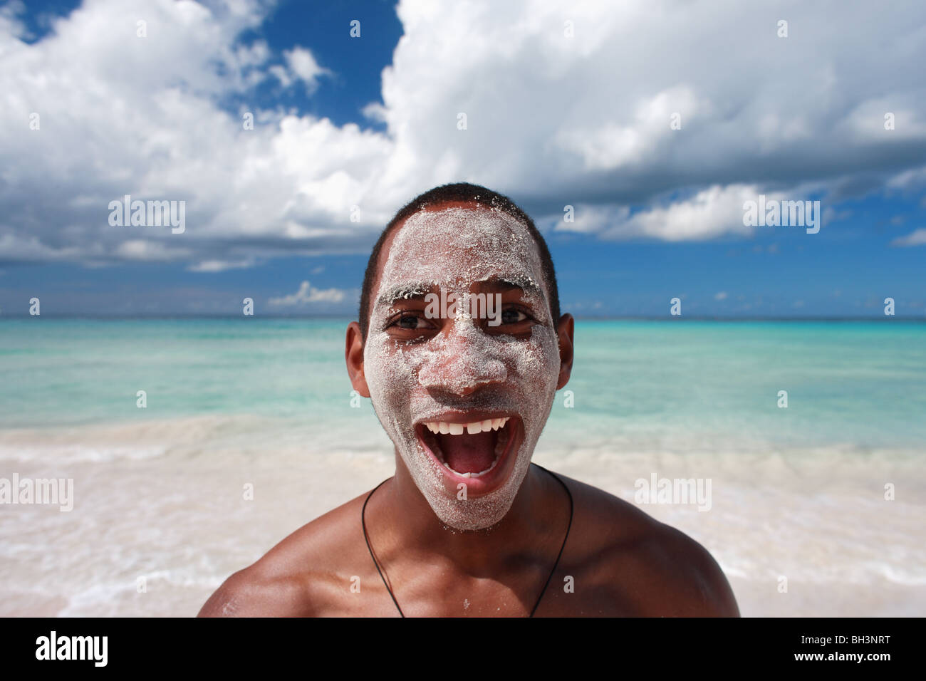 Young man on tropical beach with sand on his face, laughing Stock Photo