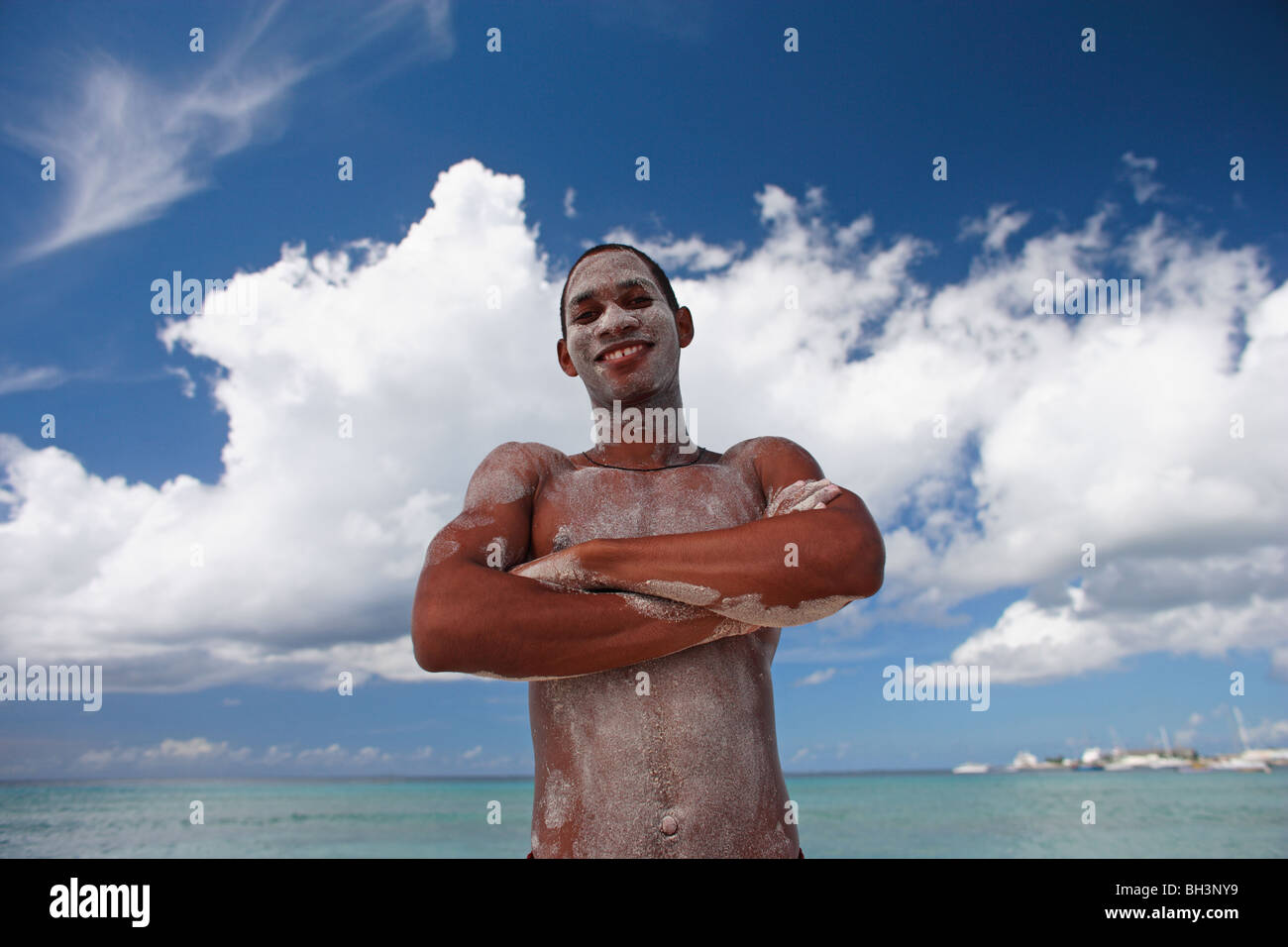 Young man standing on tropical beach with sand on his body, smiling Stock Photo