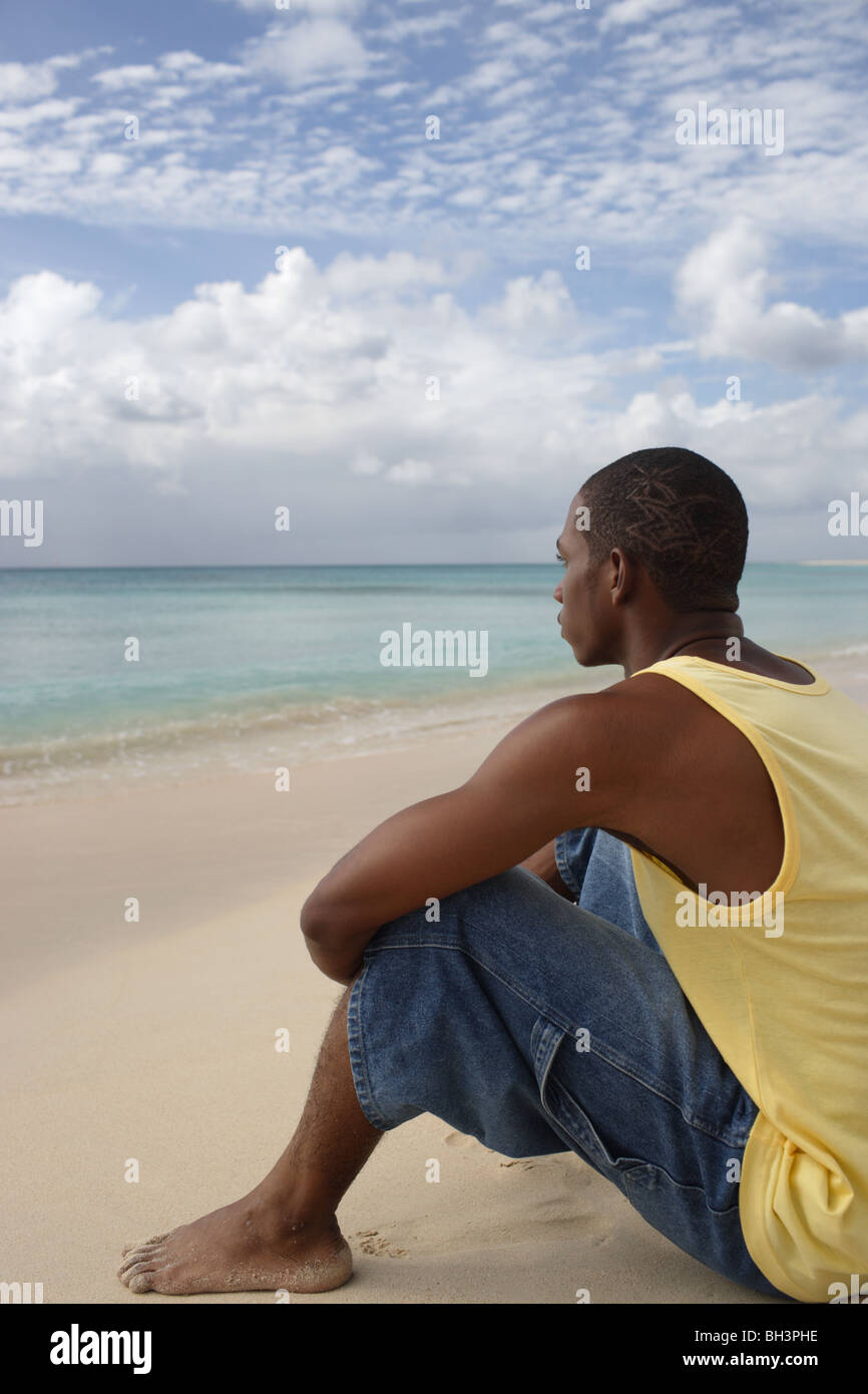 Young man sitting on a tropical beach looking out towards the sea Stock Photo