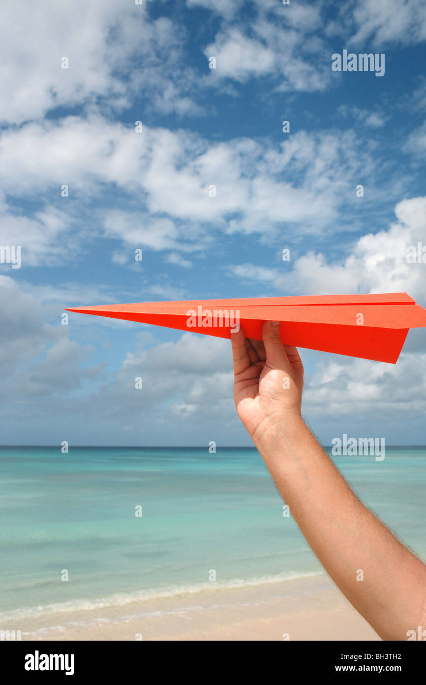 A man's hand holding a paper plane in the air on a tropical deserted beach Stock Photo