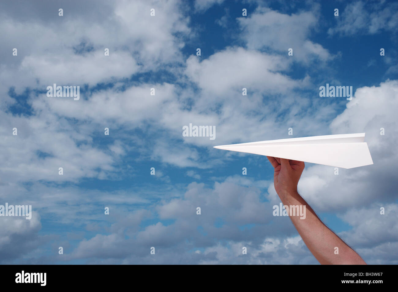 A man's hand holding a white paper airplane in a blue cloudy sky Stock Photo