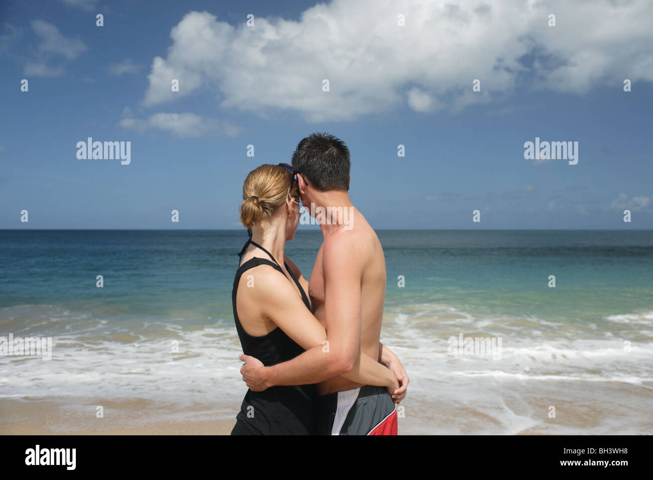 Young couple embracing looking out towards the horizon on a deserted tropical beach Stock Photo