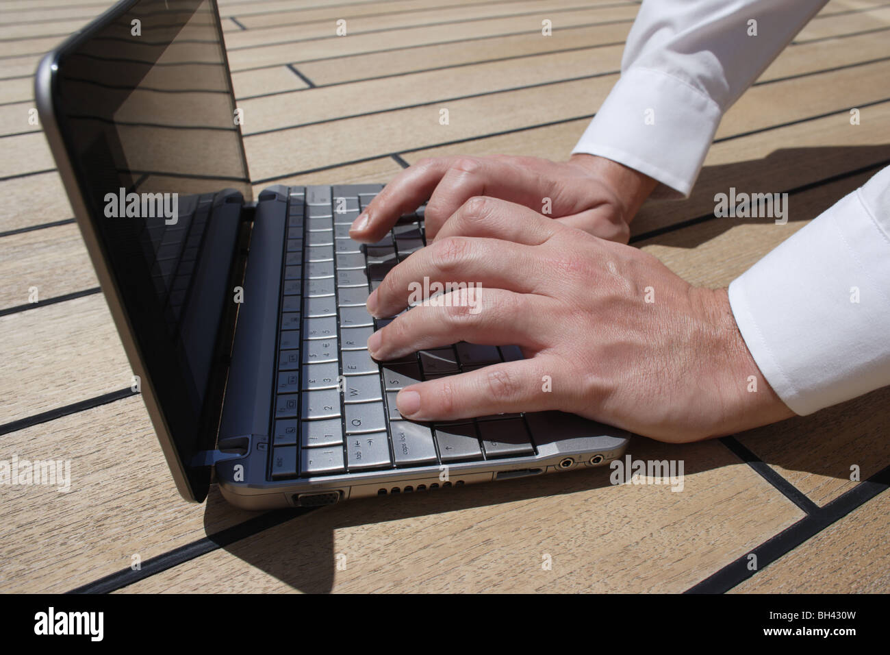 A man's hands working on a netbook computer on a wooden deck Stock Photo