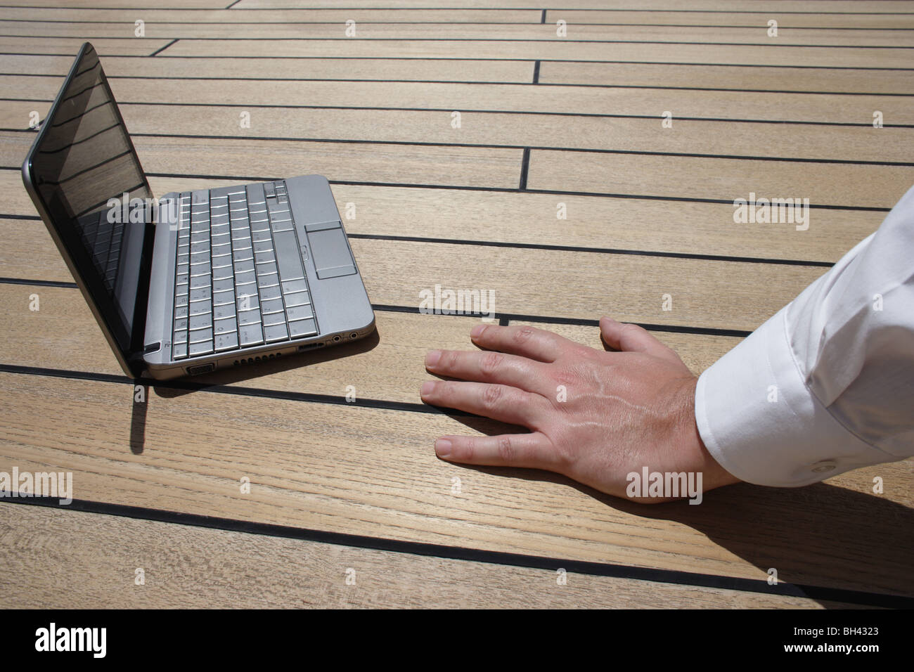 A man's hand resting next to a netbook computer on a wooden deck Stock Photo