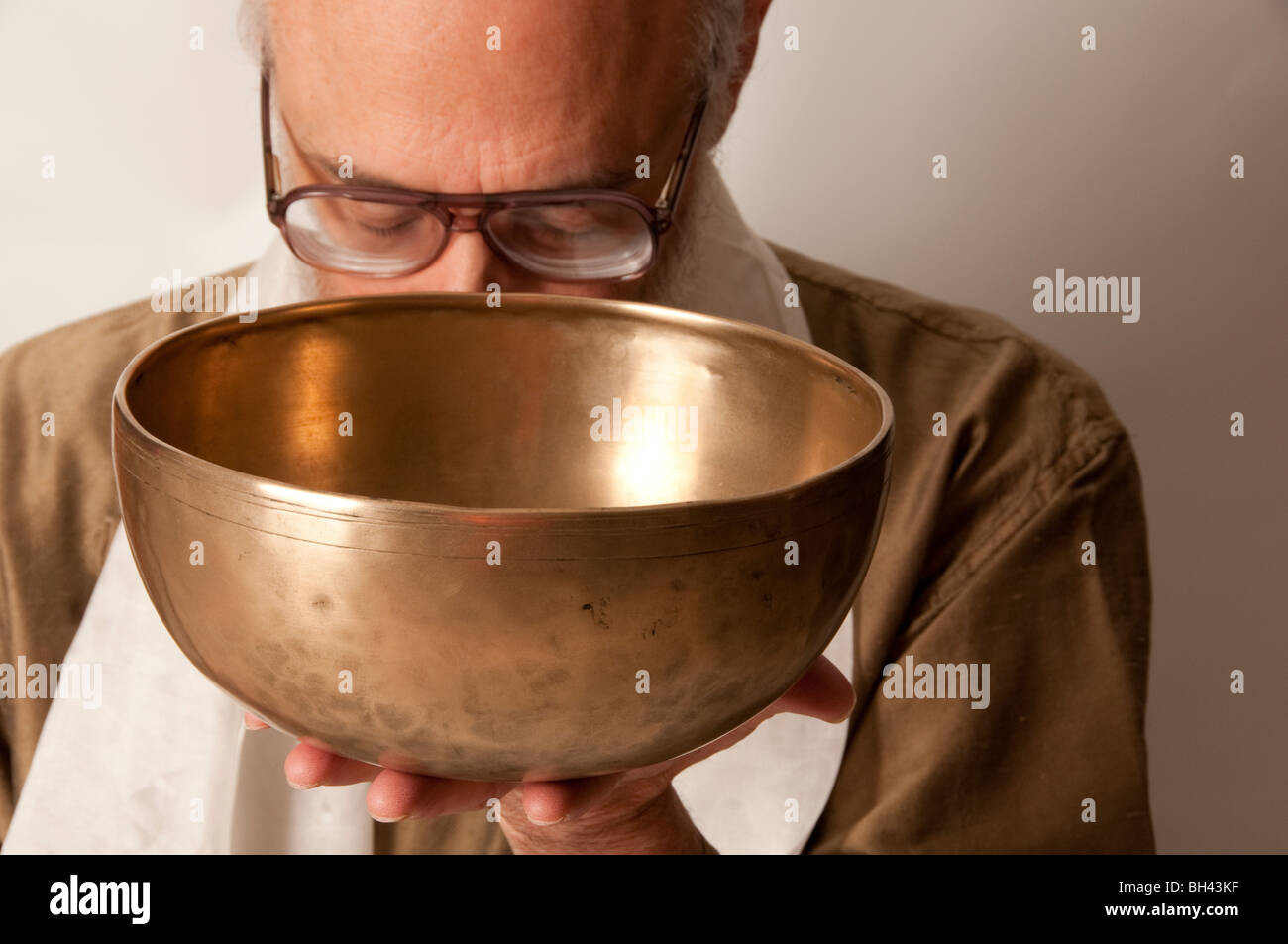 Sacred sound healing practitioner on white background with head bowed wearing glasses holding up Tibetan singing bowl Stock Photo