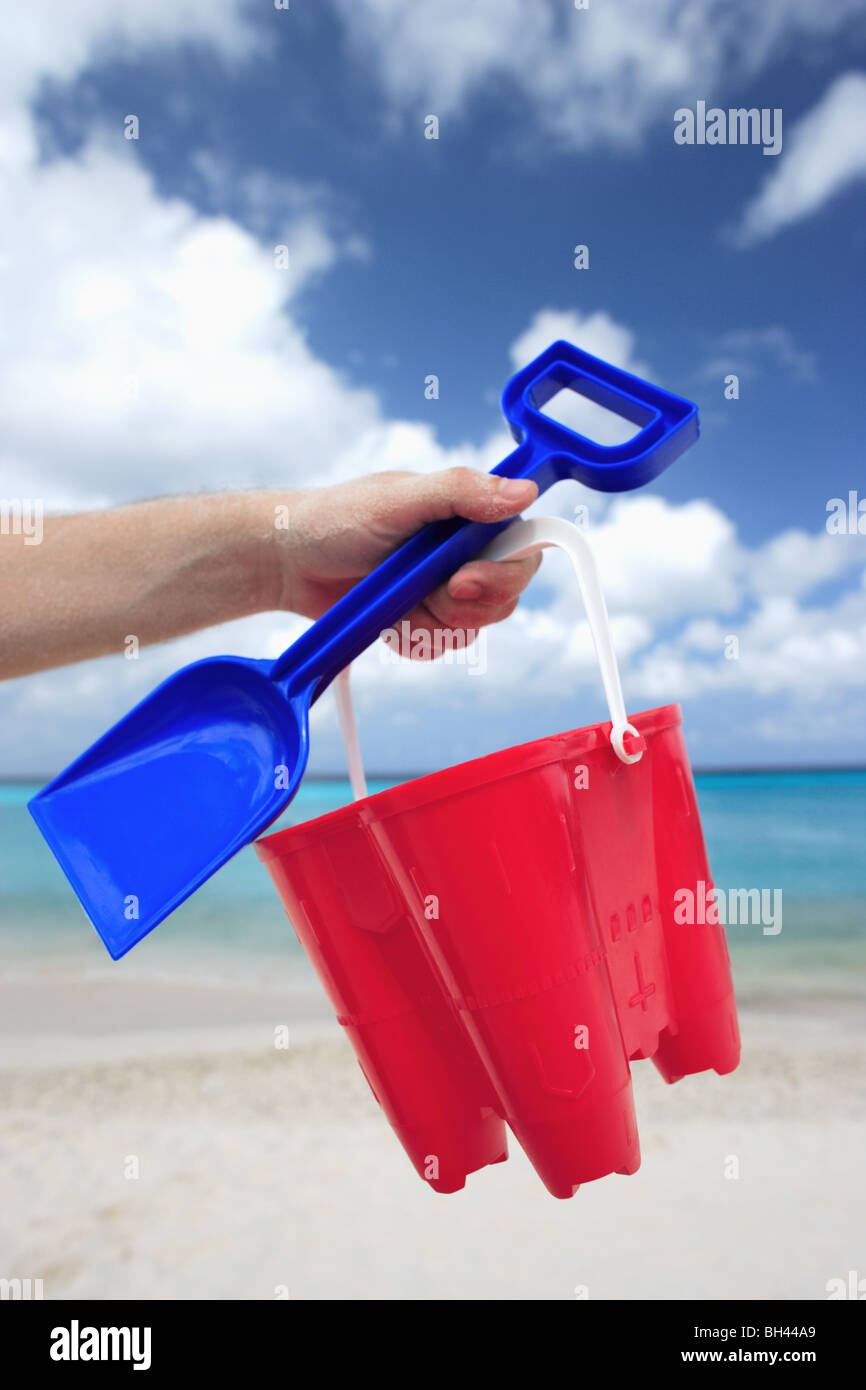 A man's hand holding a toy bucket and spade in the air on a deserted