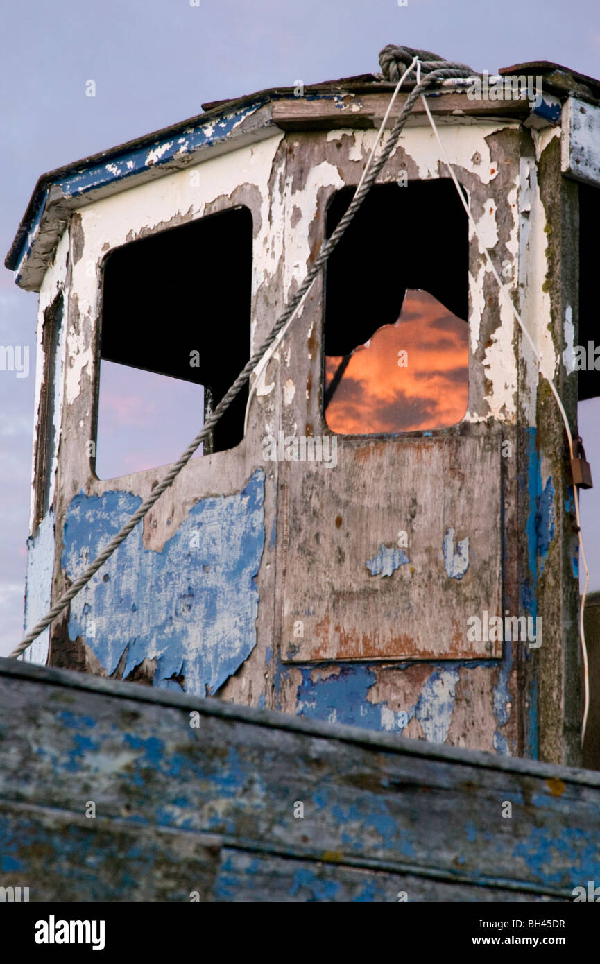 Tight crop of dilapidated boat with fiery sky reflected in smashed window. Stock Photo